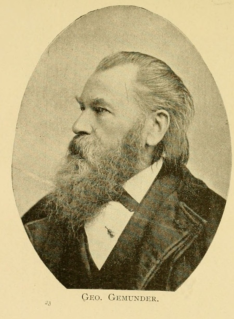 A half-length halftone photograph of an elderly man in three-quarter profile facing left, printed inside an oval whose top rises to a point. He has a long full beard going white, hair swept back from a high forehead and worn long over the ears, and a dark coat over a white wing collar and dark bow tie; a small violin-shaped stickpin is set in the shirt front. Beneath the oval, in spaced small capitals, the printed caption reads GEO. GEMUNDER. A small numeral 23 is printed low and to the left, clear of the caption. The leaf is toned cream, and the halftone screen is plainly visible across the darker areas of coat and beard.